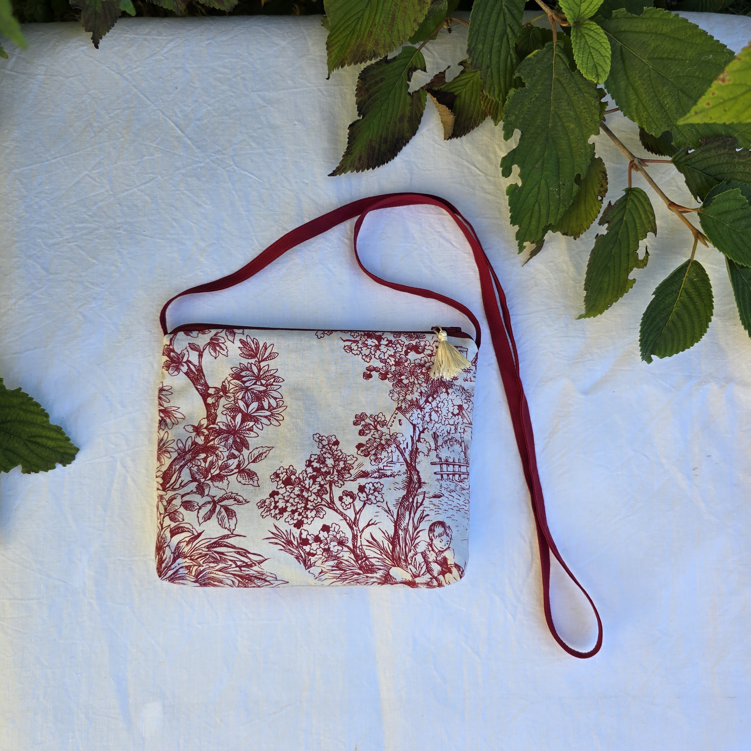Pochette avec bandouli&egrave;re en tissu toile de Jouy bordeaux et &eacute;cru agr&eacute;ment&eacute;e d'un pompon