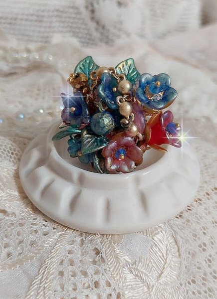 Bague Bel Air mont&eacute;e avec des fleurs lucites peintes &agrave; la main aux couleurs : Bleu, Rose, Rouge, Argent, Blanc avec feuilles ondul&eacute;es Vert Cuivr&eacute; &agrave; laquelle s&rsquo;ajoute perles Dor&eacute;es en Verre
