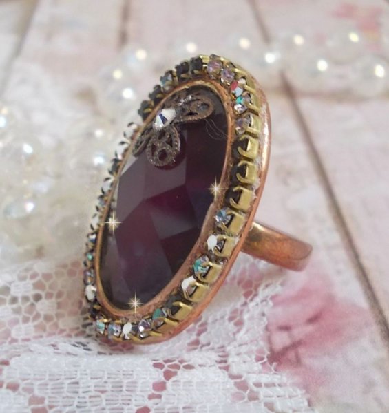 Elegante anillo burdeos creado con cristales PureCrystal, un sello en forma de flor y un cabuj&oacute;n de cristal.