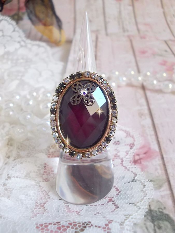 Elegante anillo burdeos creado con cristales PureCrystal, un sello en forma de flor y un cabujón de cristal.