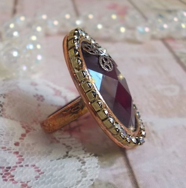 Elegante anillo burdeos creado con cristales PureCrystal, un sello en forma de flor y un cabuj&oacute;n de cristal.