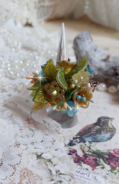 Bague C&eacute;zanne mont&eacute;e avec des petites fleurs lucites peintes &agrave; la main &agrave; laquelle s&rsquo;ajoute des feuilles, cristaux, perles, &eacute;tamines, grosses rocailles, perles nacr&eacute;es et m&eacute;tal sur une bague en Laiton