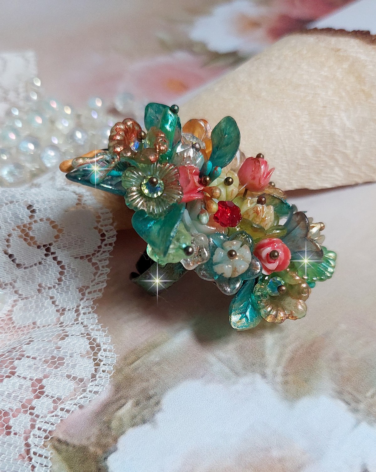 Bague Patiflo d’une composition florale créée avec des cristaux, fleurs en Résine, perles, clochettes, pensées, boutons de rose en Verre, estampes et coupelles. Le tout est monté sur une bague estampe