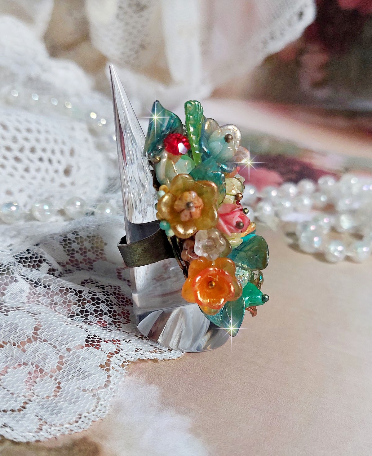 Bague Patiflo d’une composition florale créée avec des cristaux, fleurs en Résine, perles, clochettes, pensées, boutons de rose en Verre, estampes et coupelles. Le tout est monté sur une bague estampe