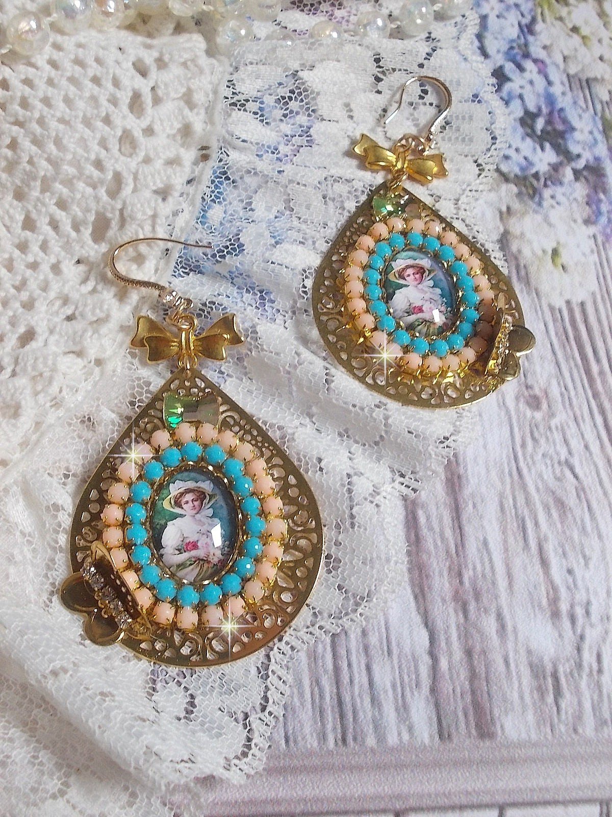 BO Mademoiselle Noellia avec des cabochons ovales représentant une femme avec un chapeau et un nœud blanc à laquelle s’ajoute des cristaux, chaînes strass Pêche et Turquoise sur crochets en plaqué Or