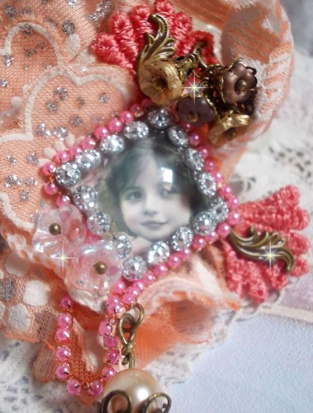 Broche Rosa r&uacute;stica creado con un cabuj&oacute;n que representa una ni&ntilde;a sonriente, strass naranja y encaje rosa, cristales, cuentas de vidrio y accesorios varios