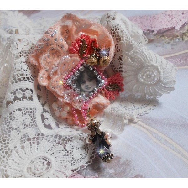 Broche Rosa r&uacute;stica creado con un cabuj&oacute;n que representa una ni&ntilde;a sonriente, strass naranja y encaje rosa, cristales, cuentas de vidrio y accesorios varios