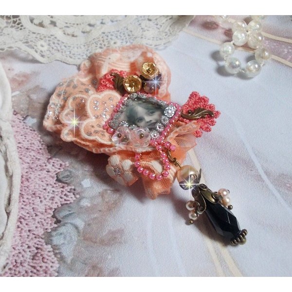 Broche Rosa r&uacute;stica creado con un cabuj&oacute;n que representa una ni&ntilde;a sonriente, strass naranja y encaje rosa, cristales, cuentas de vidrio y accesorios varios