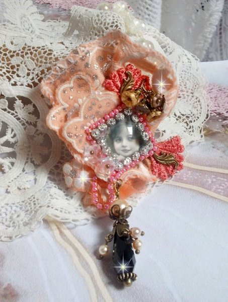 Broche Rosa r&uacute;stica creado con un cabuj&oacute;n que representa una ni&ntilde;a sonriente, strass naranja y encaje rosa, cristales, cuentas de vidrio y accesorios varios
