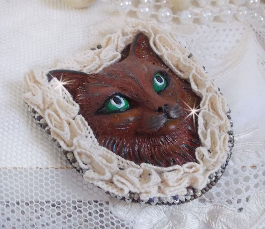 Masque Chat Rocky aux Yeux Verts tout en Fimo brodé avec un dentelle beige très fine, des perles rondes nacrées en Cristal de Swarovski, de la peinture et des rocailles