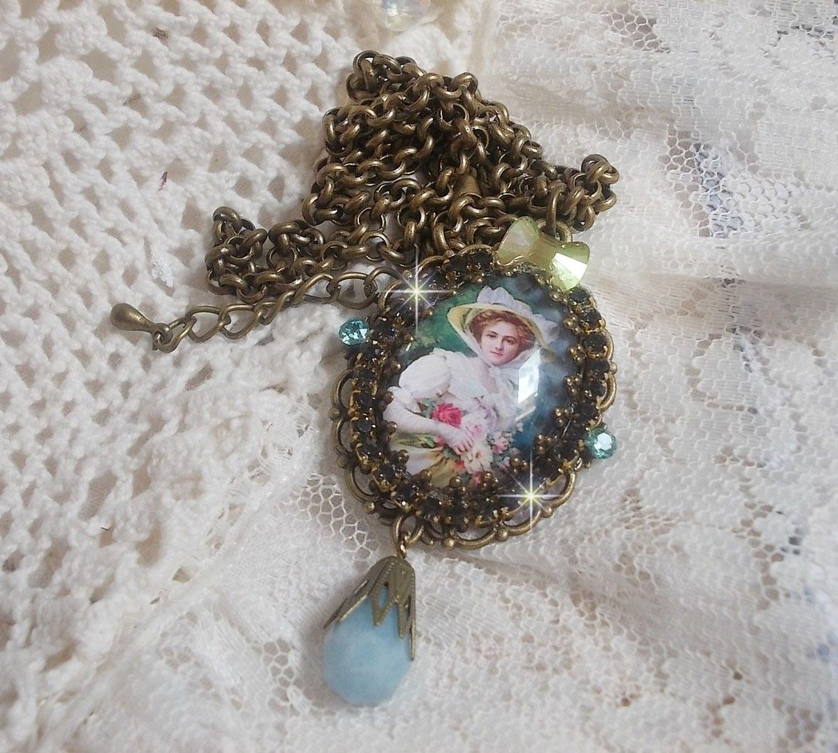 Pendentif Douce Dame créé avec un cabochon représentant une femme au chapeau blanc orné de cristaux, des accessoires de couleur Bronze et un jade teinté bleu 