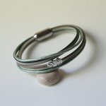 Pulsera multicuero en tonos beige, verde pálido y nacarado, decorada con una pequeña pluma
